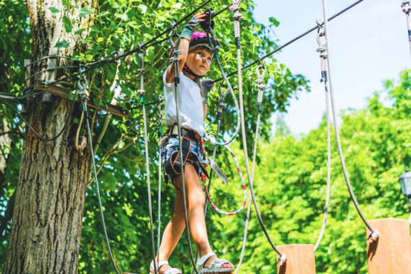 Happy 5 Year Old Girl In Pink Protective Helmet And Equipment In A Rope Park In Summer.